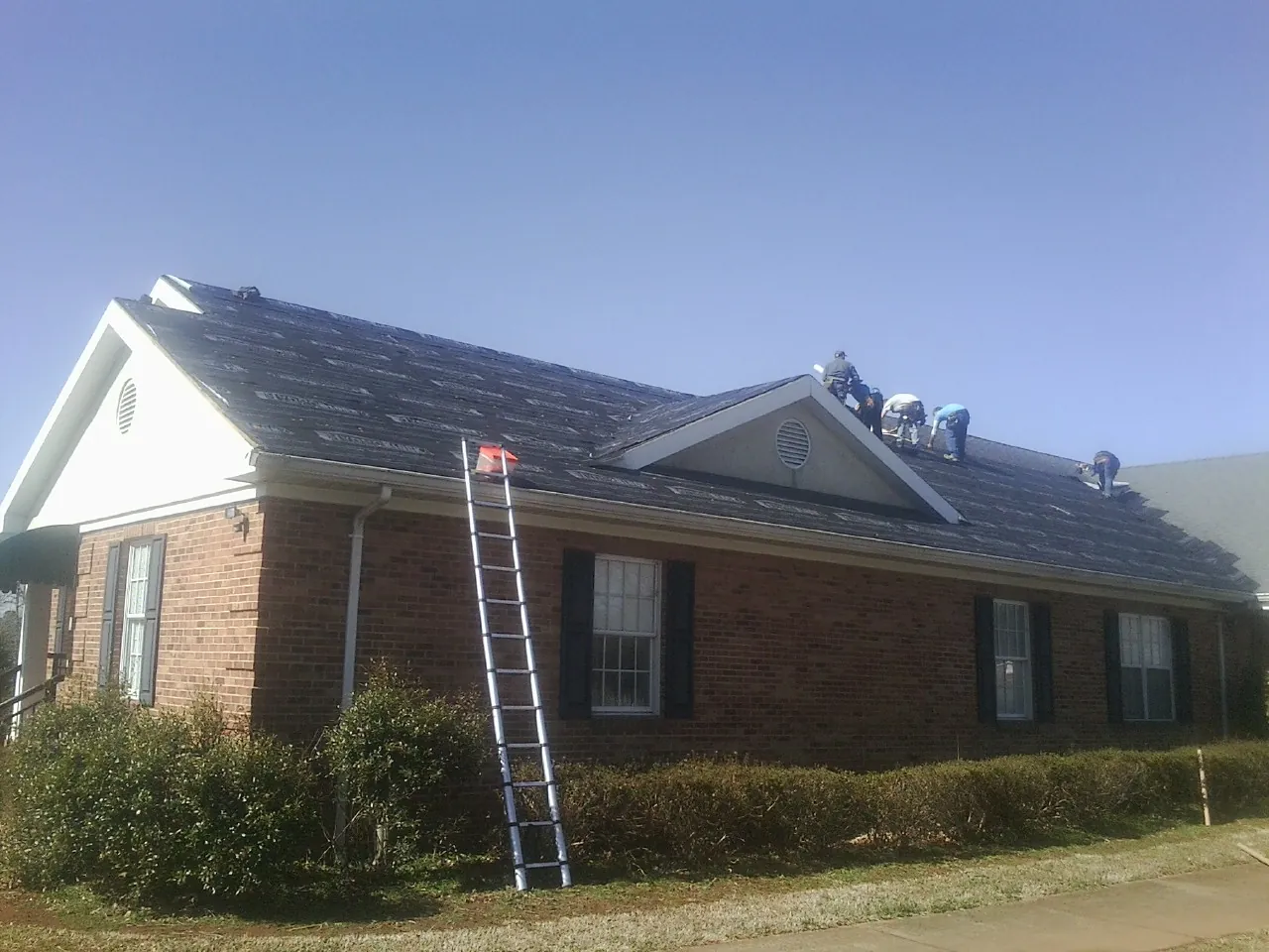 Crew tearing shingles off a brick ranch roof with a ladder set — Metal Roof Repair work by our crew in Coolville