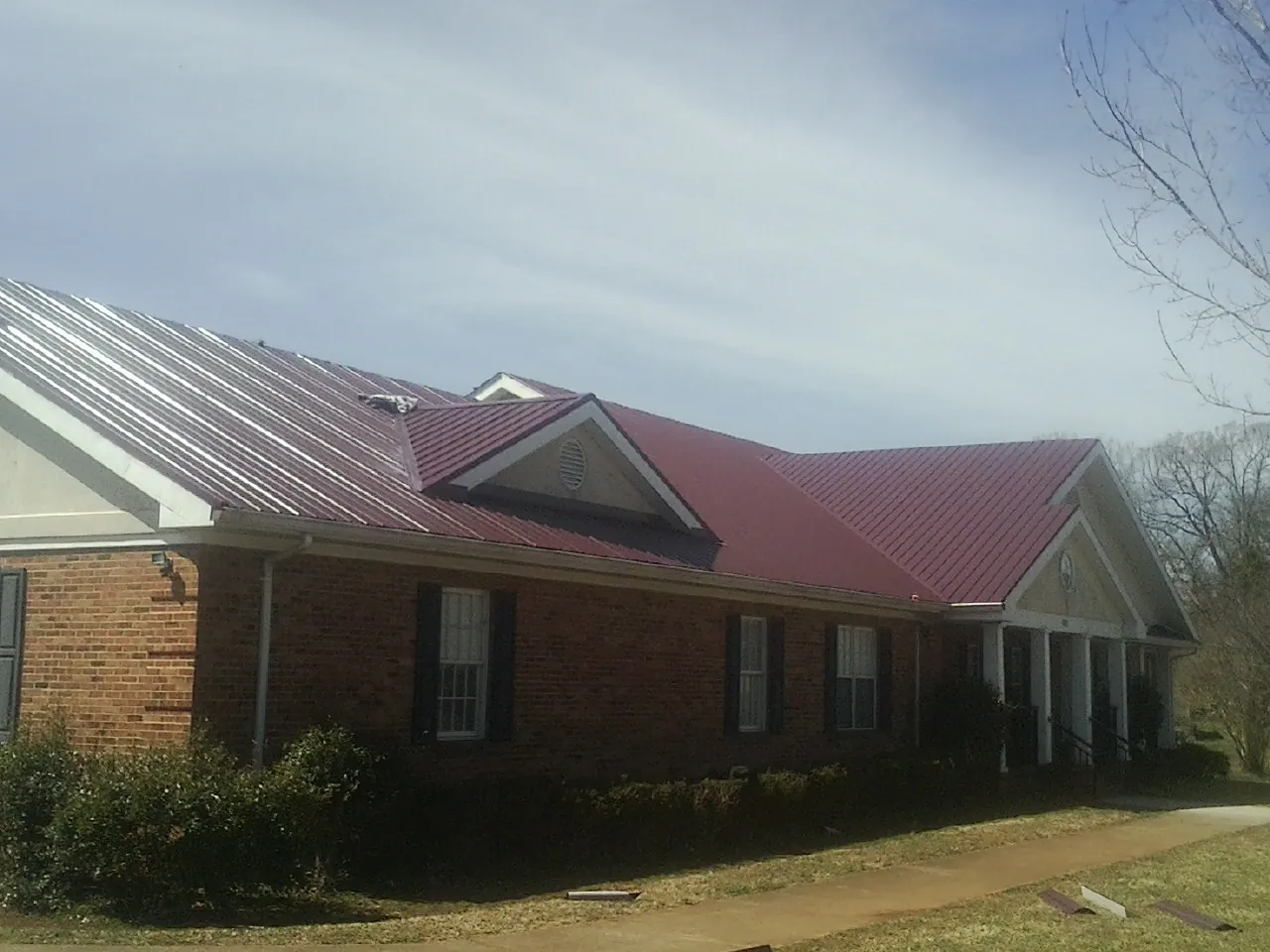Red metal roof with gabled entries on a long brick building, from a Hail Damage Roof Repair job in Coolville
