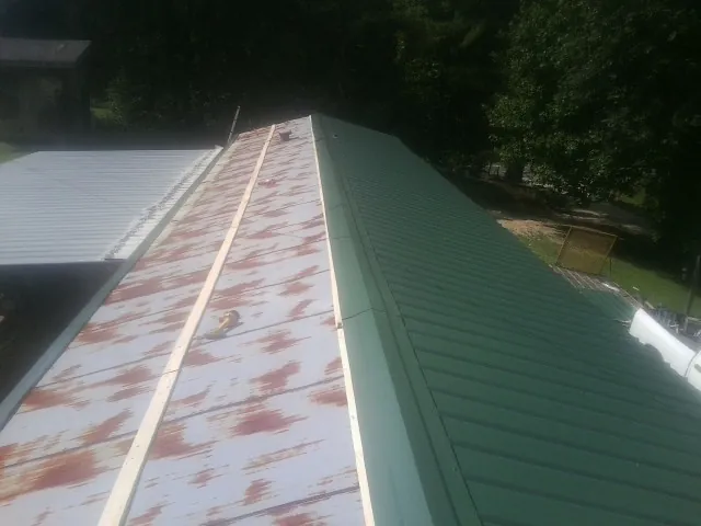 Old rusted panels beside newly installed green metal roofing — Wind Damage Roof Repair by Roofing Brothers in Coolville