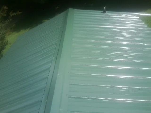 New green metal panels meeting at the ridge of a roof — Flat Roof Repair work by our crew in Coolville
