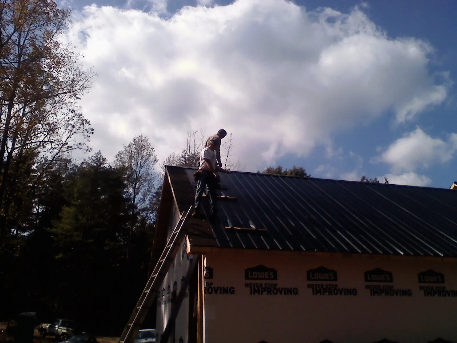 Roofer fastening dark metal panels high against a cloudy sky, from a Roof Inspection job in Coolville