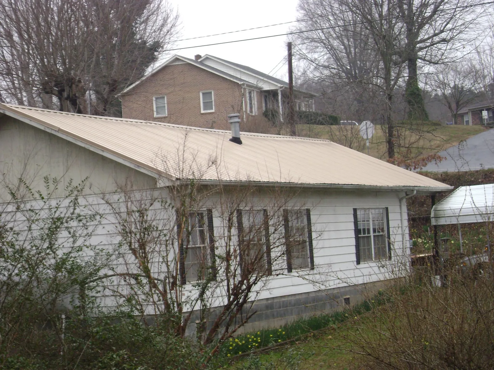 Tan metal roof on a white sided house set into a hillside — Commercial Roofing by Roofing Brothers in Coolville