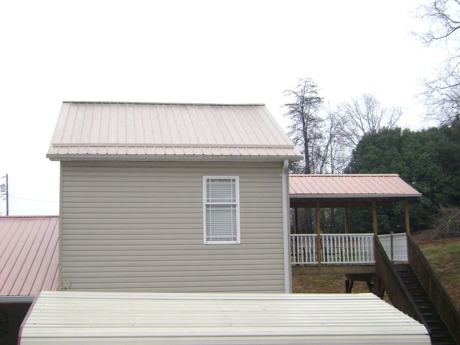 Tan metal roofs on a two story addition and attached porch, from a Roof Replacement job in Coolville